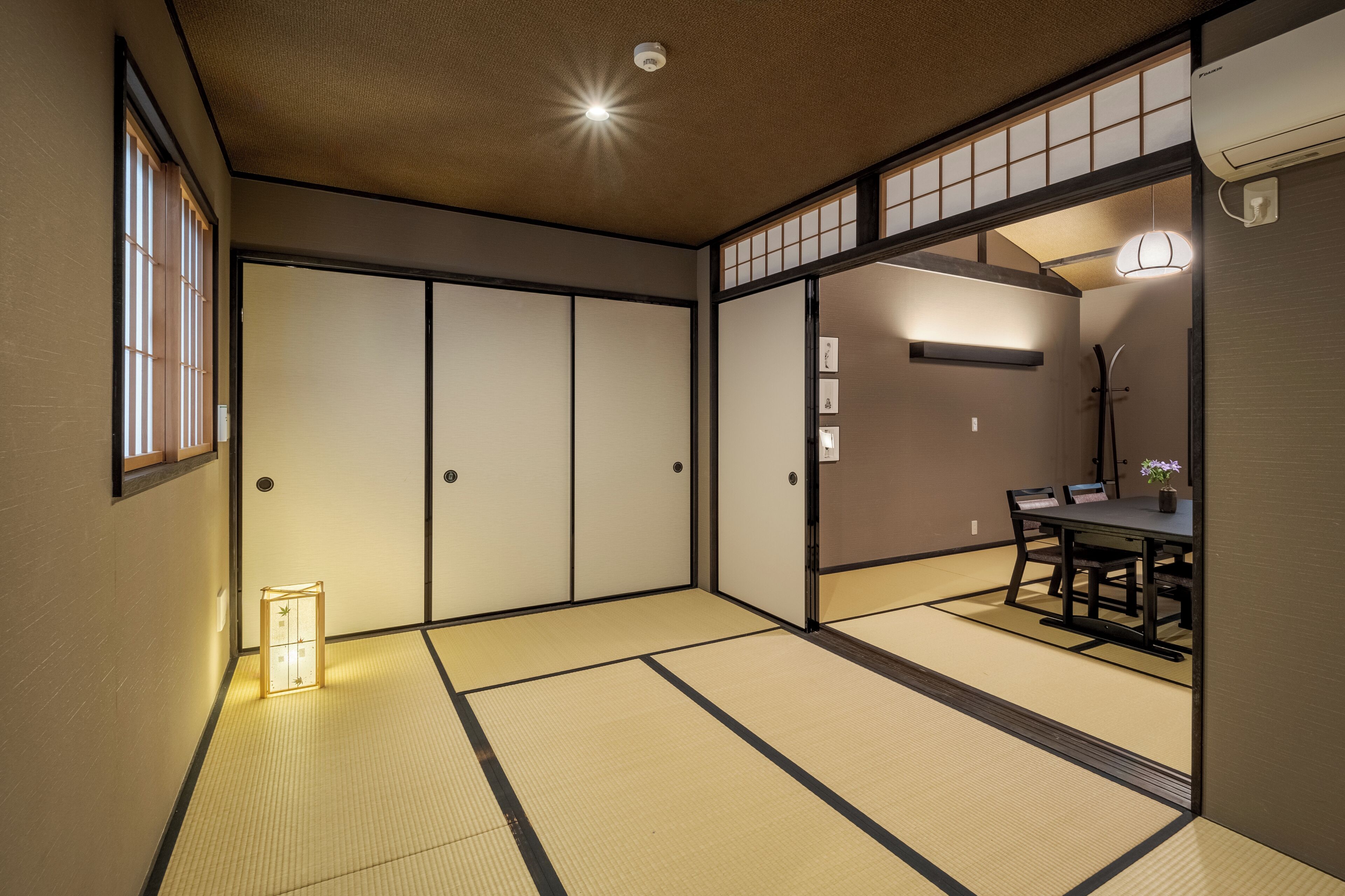 A traditional Japanese room with tatami flooring, sliding doors, a table with chairs, and a hanging light fixture.