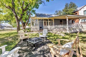 A covered patio with Adirondack chairs, a fire pit, and a white picket fence.