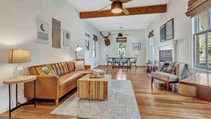 A spacious living room with a wooden floor, a ceiling fan, a fireplace, and a dining area with a table and chairs.