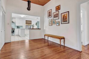 A spacious room with a wooden floor, a bench, and a kitchen visible through an open door. - Ferien Haus - Hot Tub, Fire Pit & Walk to Main St (Fredericksburg)
