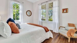 A bedroom with a bed, a chair, a window, and a picture on the wall.