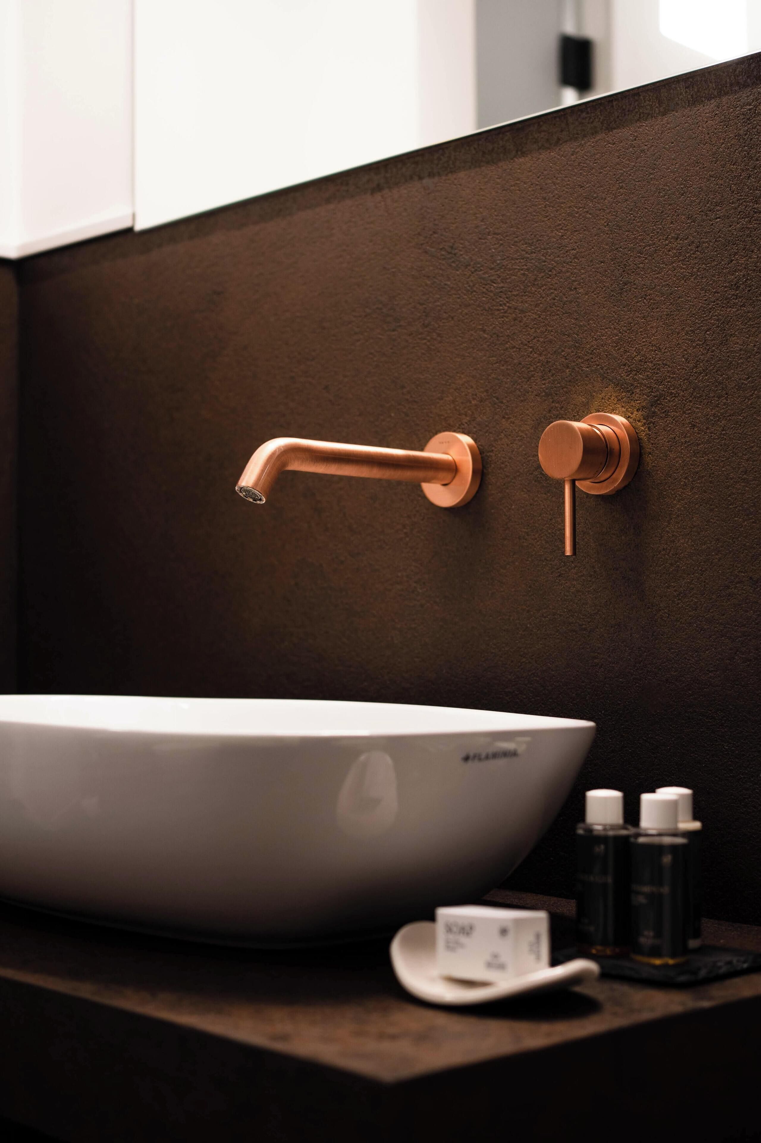A bathroom with a white sink, copper faucet, and a dark textured wall.