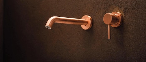 Un baño con lavamanos blanco, grifo de cobre y pared oscura con textura.