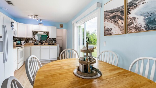 A kitchen with white cabinets, a wooden dining table with chairs, and a large window with a view of the outdoors. - Charming 3BR Home with Free Parking & Game Room (Panama City)