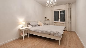 Un dormitorio con cama, mesita de noche, lámpara y ventana con cortinas.