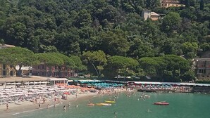 A beach with umbrellas and people, a boat, and a hill with buildings. - Rapallo 2-bed Apt, Sleeps 5 With Hot Tub (Rapallo)