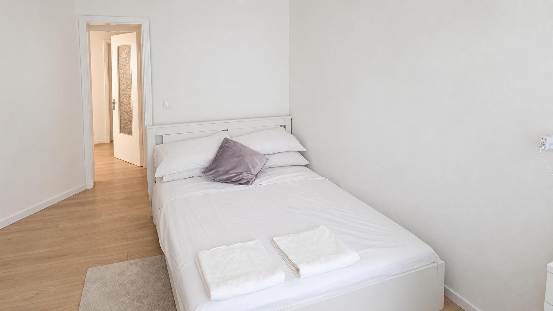 A single-bed room with a white headboard, a grey pillow, and two folded white towels on the bed.