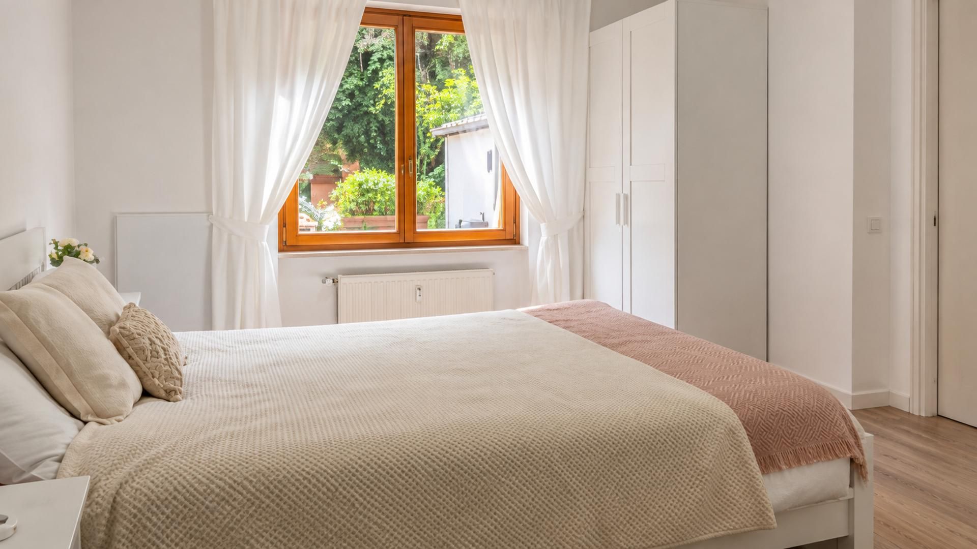 Quarto com cama, janela com cortinas, radiador e guarda-roupa.