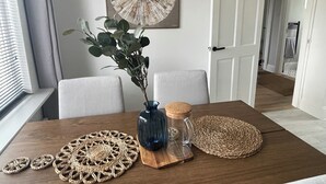 Uma mesa de jantar com um vaso de plantas verdes, um pote de vidro e jogos americanos trançados.