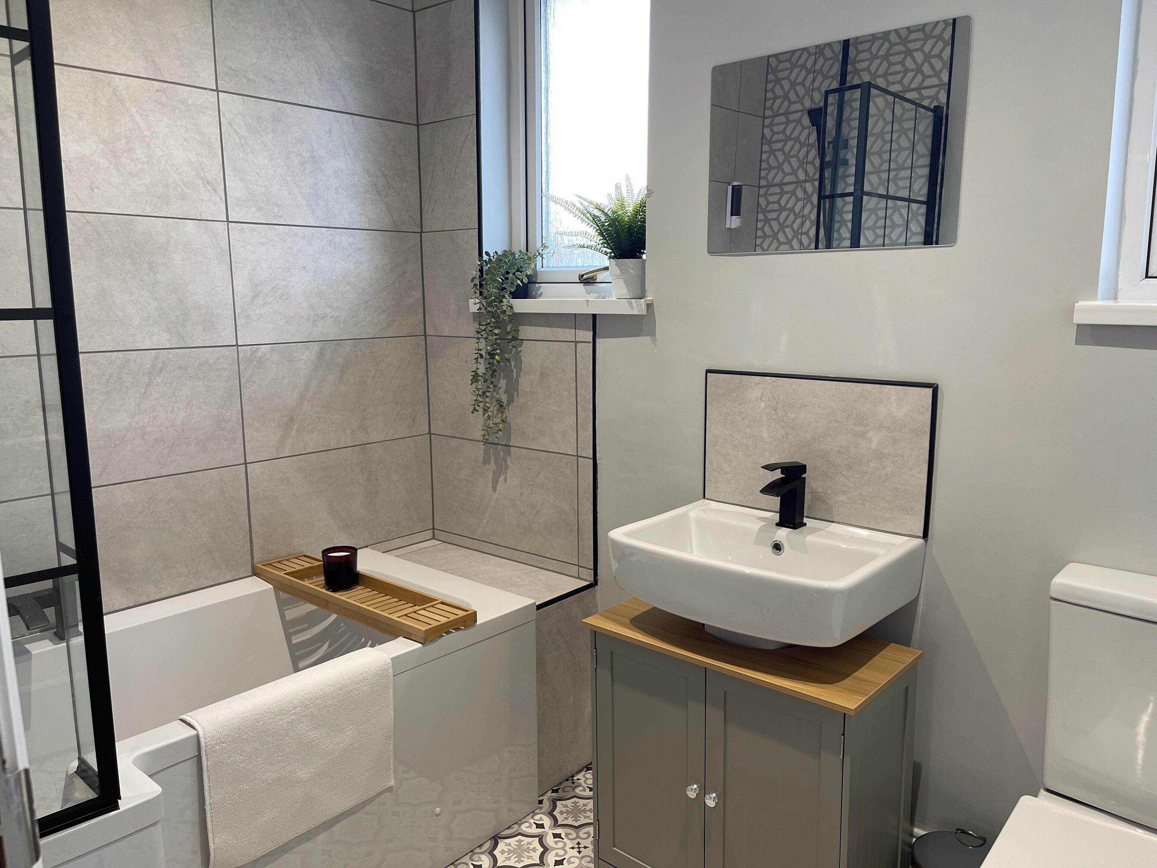 A modern bathroom with a shower, a sink, and a toilet. There is a plant on the windowsill and a towel hanging on the wall.