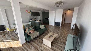Un salon moderne avec un canapé vert, une table basse et un coin repas comprenant une table et des chaises blanches.