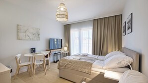 A modern hotel room with a bed, a desk with a chair, a television, and a large window with curtains.