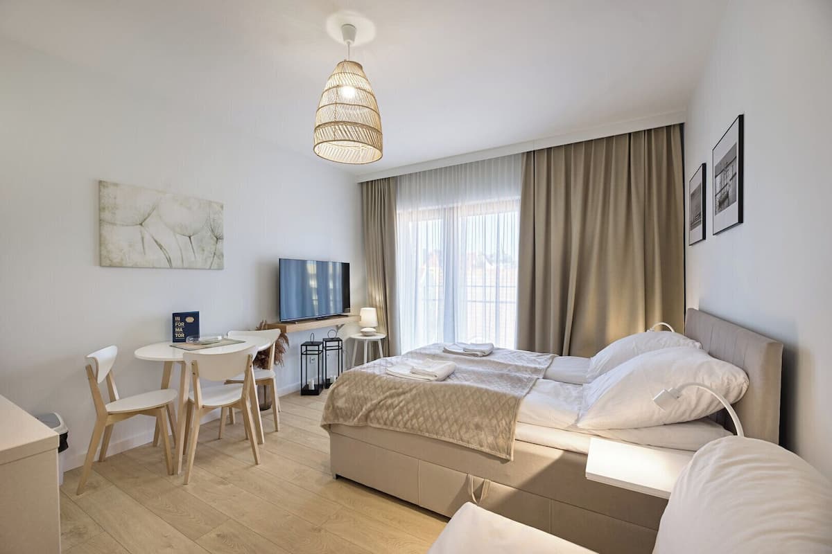 Ein modernes Hotelzimmer mit einem Bett, einem Schreibtisch mit Stuhl, einem Fernseher und einem großen Fenster mit Vorhängen.