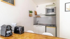 Cocina compacta con microondas, tostadora y cafetera sobre la encimera, un lavamanos y un reloj en la pared.