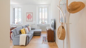 A living room with a grey sofa, a wooden coffee table, and a TV. There are windows with white frames and a red elephant poster on the wall. - Rooftop Nest in Como City Center (Como)