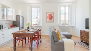 A modern kitchen with white cabinets, a wooden dining table, and red chairs. There is a large window providing natural light and a view of the outside. - Rooftop Nest in Como City Center (Como)