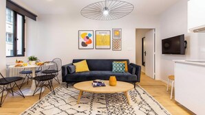 A modern living room with a dark blue sofa, a round coffee table, and a dining area with a white table and black chairs.