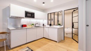 A modern kitchen with white cabinets, a microwave, and a sink. There is a small dining area with a chair and a rug.