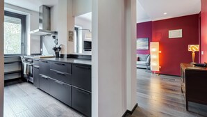 Una cocina moderna con armarios oscuros y electrodomésticos de acero inoxidable, un ventanal grande y una pared roja de acento en la zona de estar contigua.
