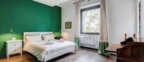 A bedroom with a bed, nightstands, a window with curtains, and a view of greenery outside.