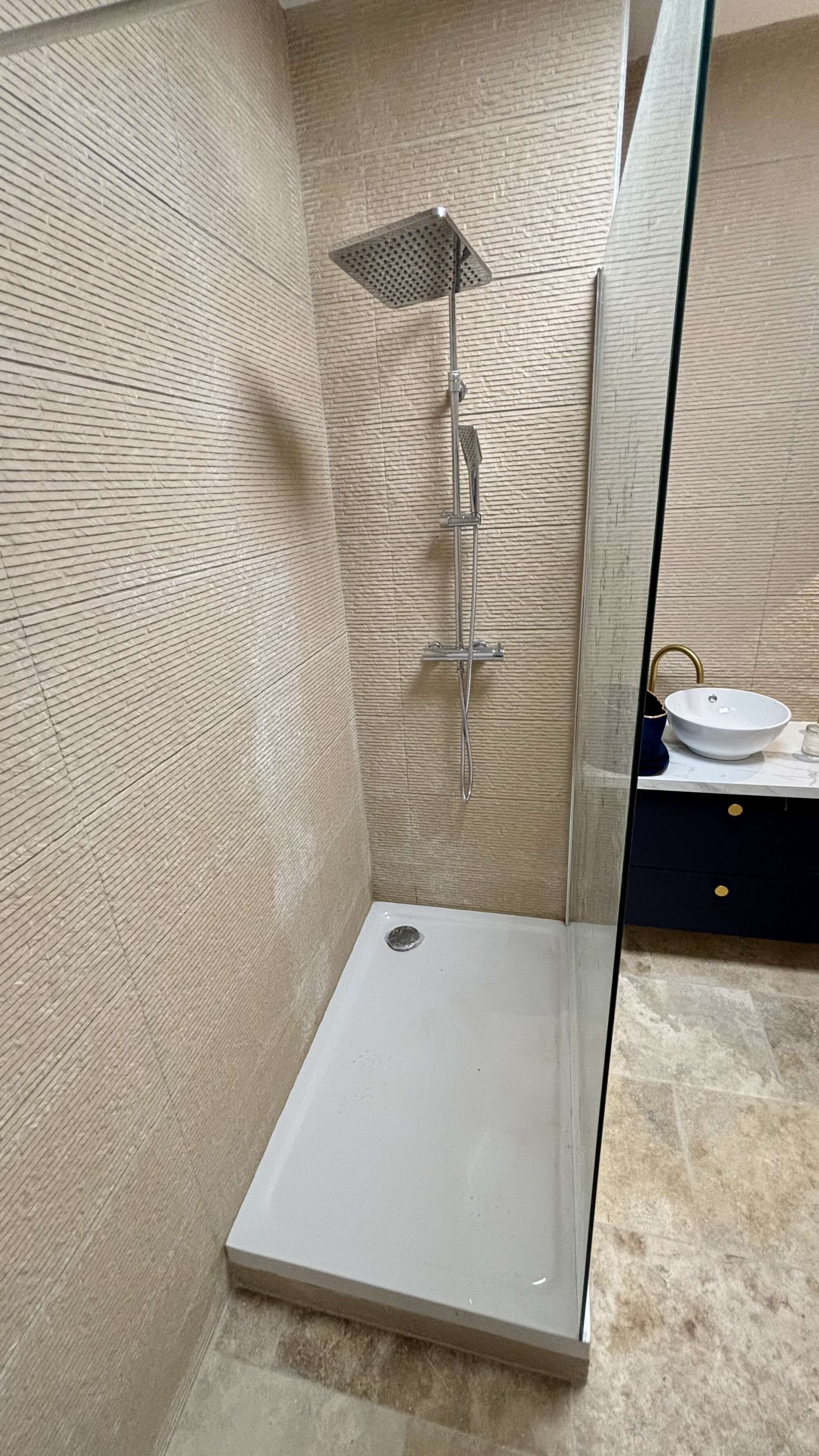 A modern bathroom with a glass-enclosed shower, a white sink, and a marble-tiled floor.