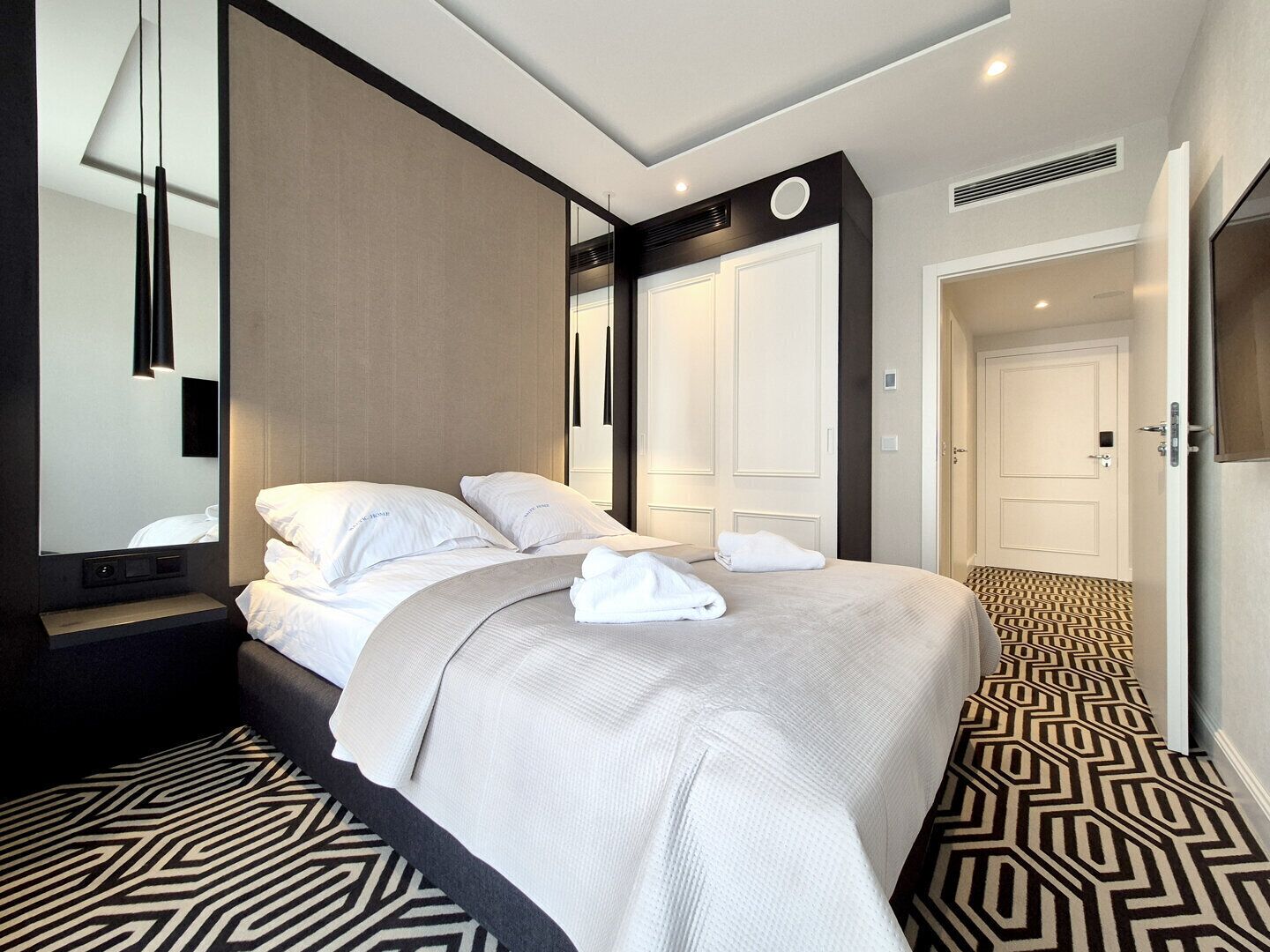 Una habitación de hotel moderna con una cama grande, un espejo, una mesita de noche y una alfombra estampada.