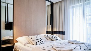 A hotel room with a bed, a mirror, a nightstand, and a window with curtains. - Fort by Baltic Home (Swinoujscie)