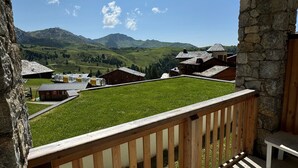 A balcony with a stone wall and wooden railing overlooking a green field and a village with traditional houses. - Ski-in/Ski-out Apt for 6 with Pool, Spa & Parking - Belle Plagne High (Belle Plagne)