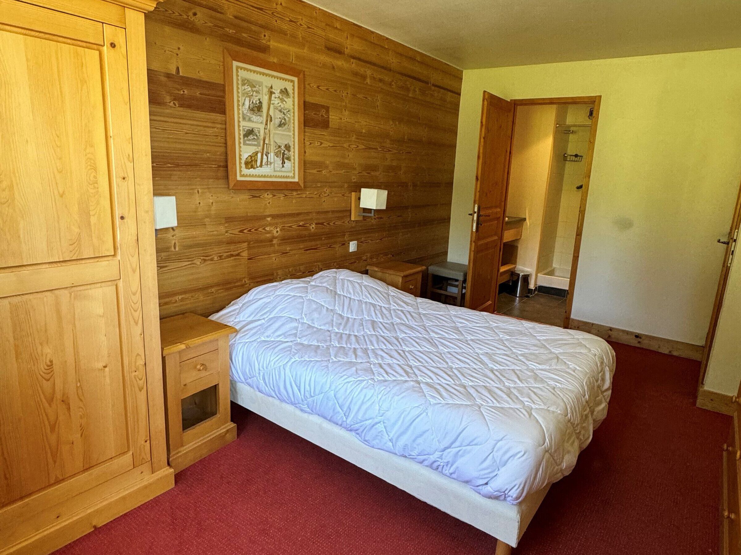 A wooden-paneled bedroom with a bed, nightstands, a mirror, and a wall-mounted picture.