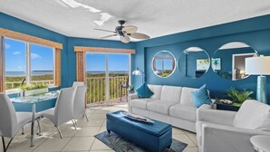 A modern living room with a white sofa, blue ottoman, and a dining area with white chairs. - Beach Retreat 2 Bedroom Ocean View, Pool & Beach (Tavernier)
