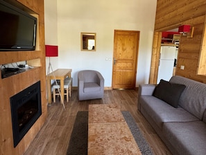 Uma sala de estar aconchegante com televisão, lareira, sofá e uma mesa pequena com cadeiras.