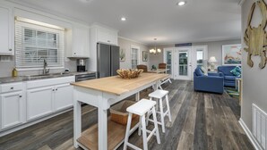 Una cocina moderna con armarios blancos, una isla de madera y un comedor con sofás azules.