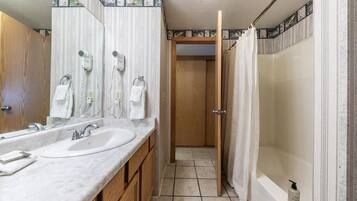 A bathroom with two sinks, a shower, and a door leading to another room.
