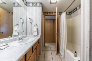 A bathroom with two sinks, a shower, and a door leading to another room.