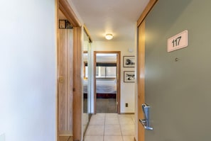 A hotel hallway with a door labeled '117' leading to a room with a bed and a window.