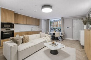 Ein modernes Wohnzimmer mit einer Couch, einem Couchtisch und Blick auf die Straße durch ein großes Fenster.
