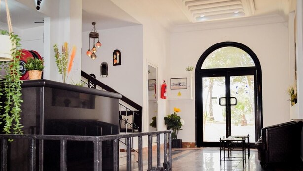 Un vestíbulo amplio con un mostrador de recepción negro, una escalera y un gran arco de entrada que da al exterior.
