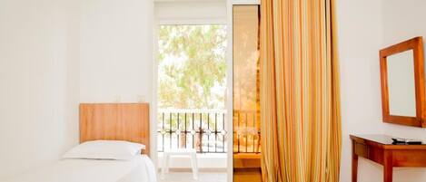 Habitación de hotel con dos camas individuales, cabecera de madera, una mesita pequeña de madera, un espejo y una puerta corrediza de cristal que da a un balcón exterior.