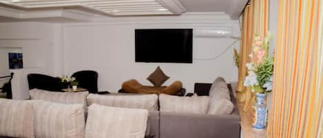 A modern living room with a sectional sofa, a flat-screen TV mounted on the wall, and a decorative vase with flowers on a side table.