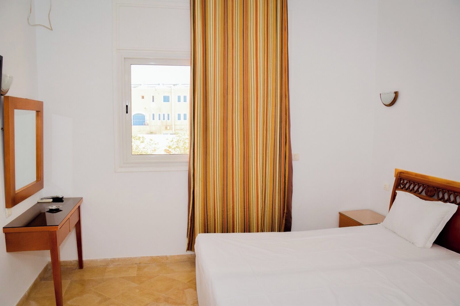 Una habitación de hotel con cama, mesita de noche, espejo, ventana y cortina.