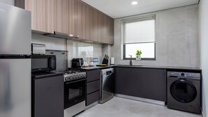 Eine moderne Küche mit Edelstahlgeräten, inklusive Backofen, Mikrowelle und Geschirrspüler, sowie ein großes Fenster mit Jalousien.