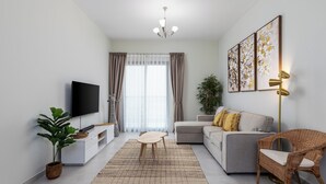 Ein modernes Wohnzimmer mit Flachbildfernseher, einer Couch, einem Couchtisch, einem Korbstuhl und einem großen Fenster mit Vorhängen.