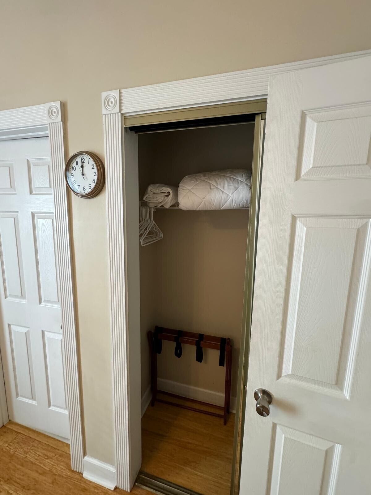 A narrow hallway with a white door on the left and a white door on the right. A clock is mounted on the wall to the left of the door.