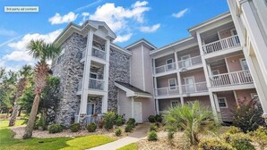 A multi-story residential building with balconies, a stone facade, and a well-maintained lawn. - Amazing 1BR condo on the ground floor (Myrtle Beach)