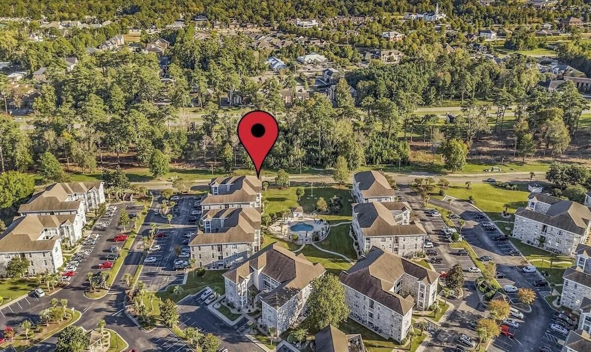 An aerial view of a residential area with multiple stone buildings, a central swimming pool, and a red location marker.