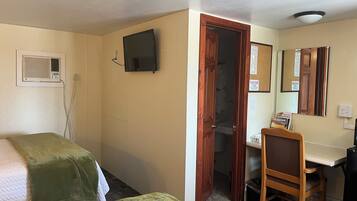 Habitación de hotel con dos camas, un escritorio, una silla, un televisor, un espejo y una puerta que da a otra habitación.