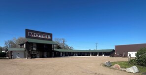 Un motel avec une enseigne bien visible, de nombreuses chambres, un parking couvert et un terrain en terre.
