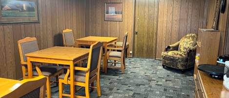 A room with a wooden table and chairs, a patterned armchair, a dresser, and a door.