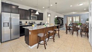 A modern kitchen with dark cabinets, stainless steel appliances, and a central island with bar stools. - Large retreat w/ pvt pool & cinema (Kissimmee)