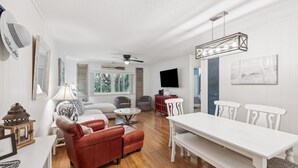 A spacious living room with a red leather sofa, white dining table, and a ceiling fan. - 148 Island House @ Forest Beach | Walk to Beach | Pool | Pet-Friendly | Tennis (Hilton Head Island)